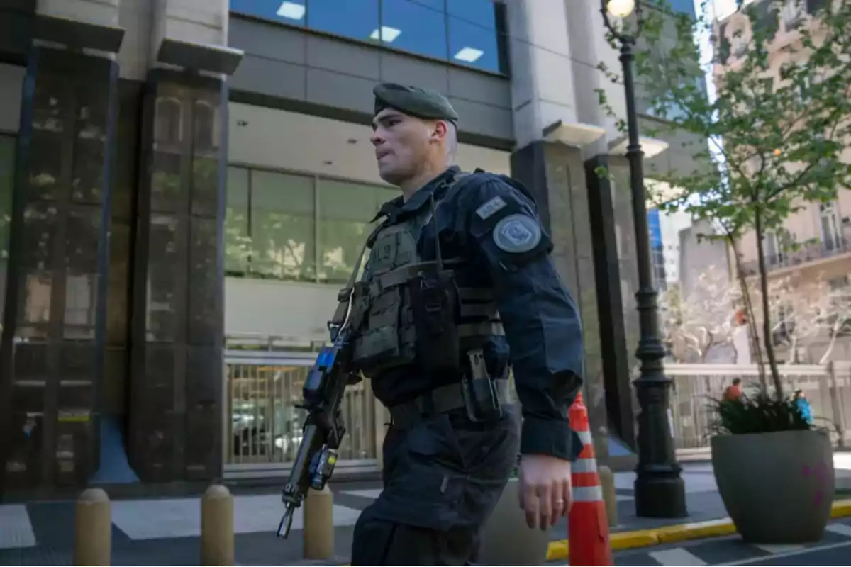 Un oficial de seguridad camina por una calle urbana con un edificio de oficinas de fondo.