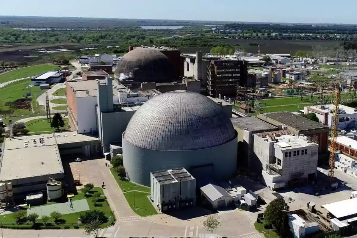 Vista aérea de una planta nuclear con dos grandes cúpulas y varias edificaciones circundantes, rodeada de áreas verdes y caminos.