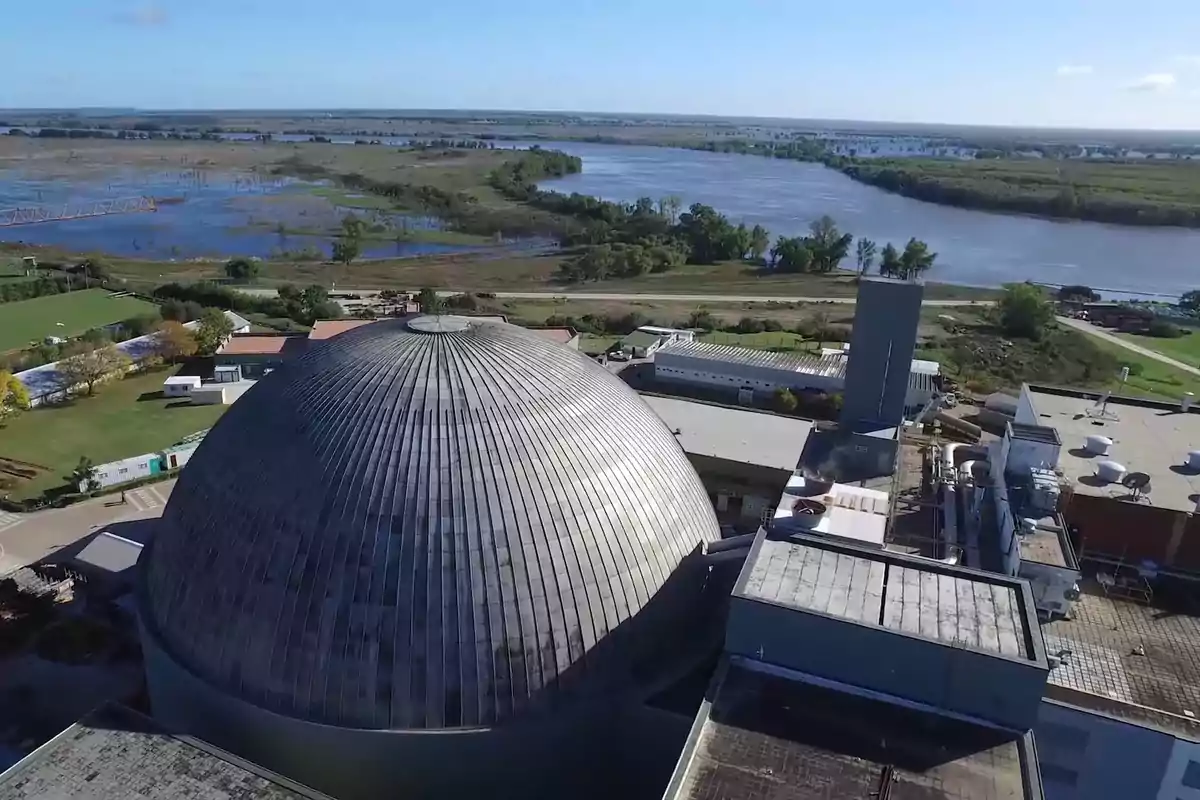 Vista aérea de una planta industrial con un edificio de cúpula metálica y un río en el fondo.