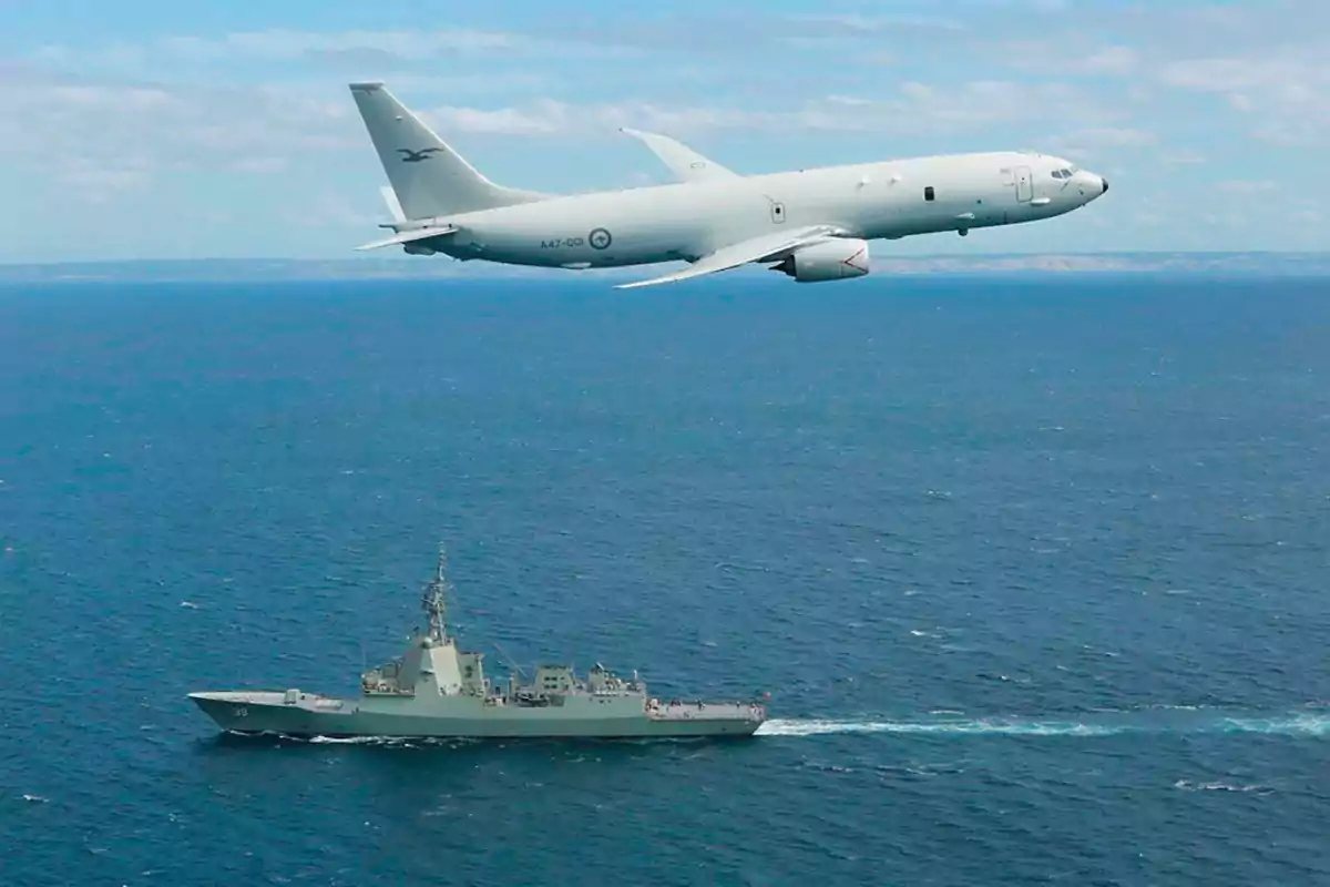 A military plane flying over a ship in the ocean.