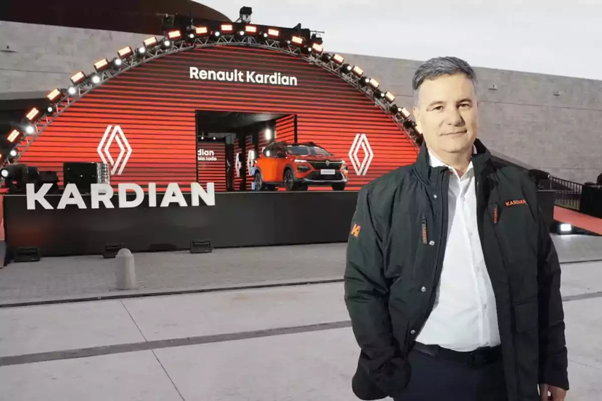 Un hombre de pie frente a una exhibición de Renault Kardian con un coche naranja en el fondo.