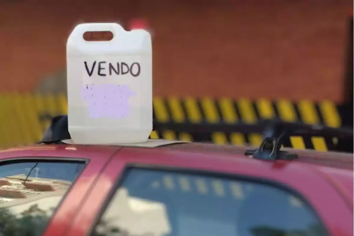 Un bidón blanco con la palabra "VENDO" escrito en él, colocado sobre el techo de un automóvil rojo.