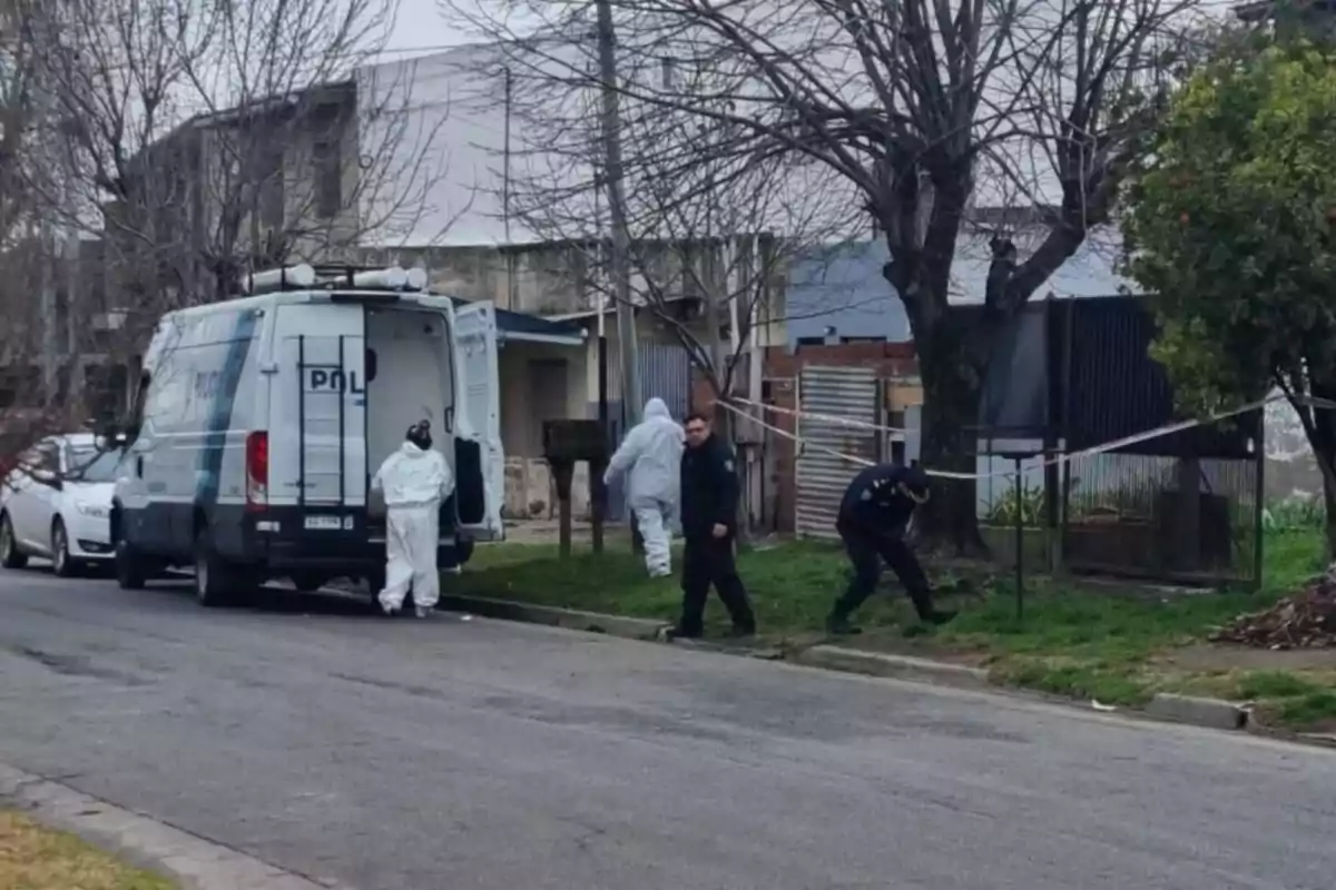 Investigadores forenses y policías trabajan en la escena de un crimen en un vecindario, con una camioneta de la policía estacionada cerca.