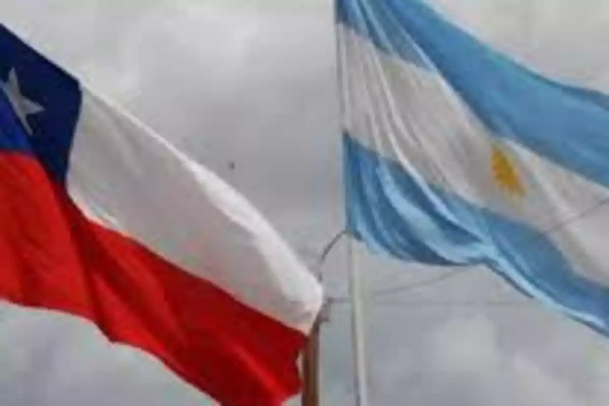 Banderas de Chile y Argentina ondeando juntas en el cielo nublado.