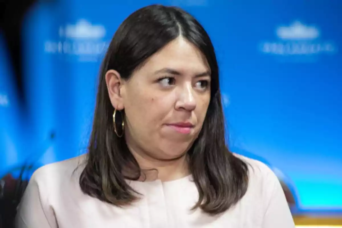 Mujer con cabello oscuro y aretes grandes frente a un fondo azul.