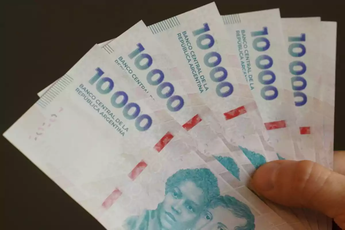 Una mano sosteniendo varios billetes de 10,000 pesos argentinos.