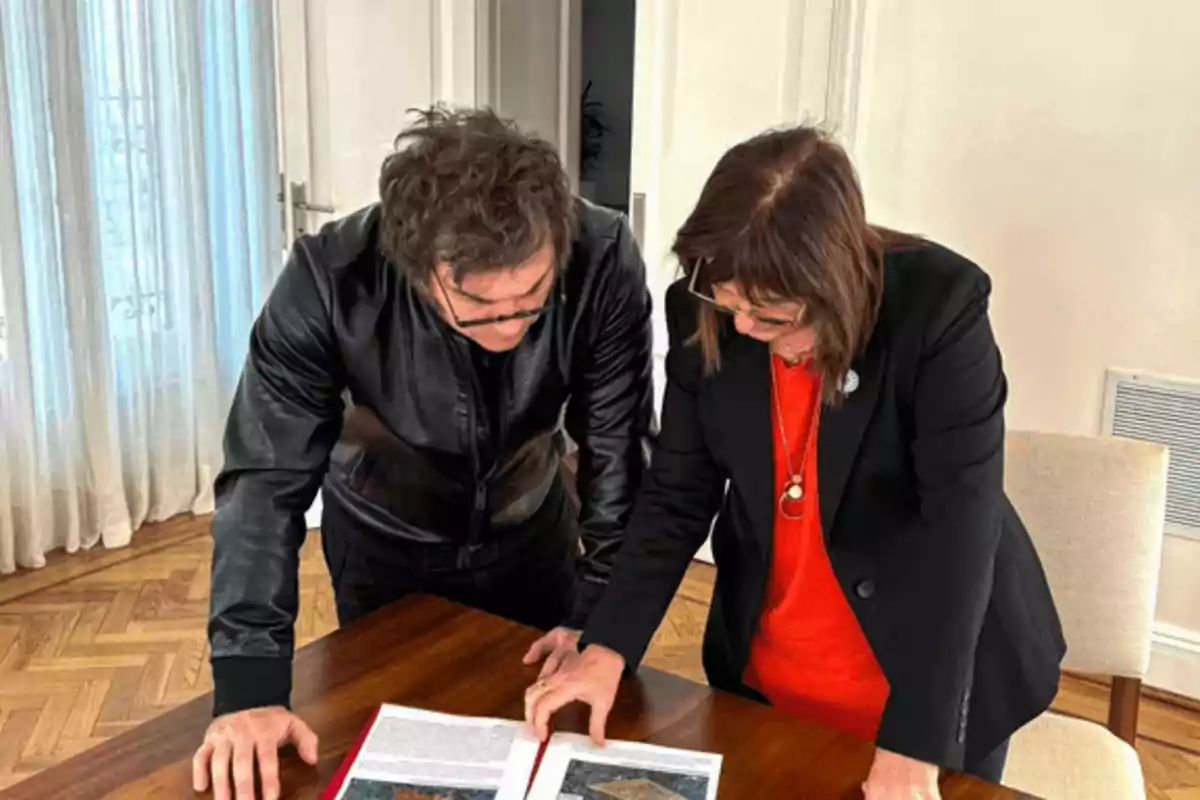 Dos personas revisan un documento en una mesa de madera en una habitación iluminada.