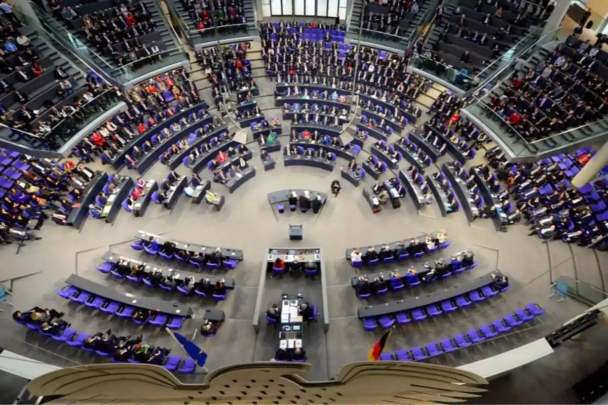 Vista aérea de un parlamento con asientos dispuestos en forma semicircular y personas sentadas en ellos.