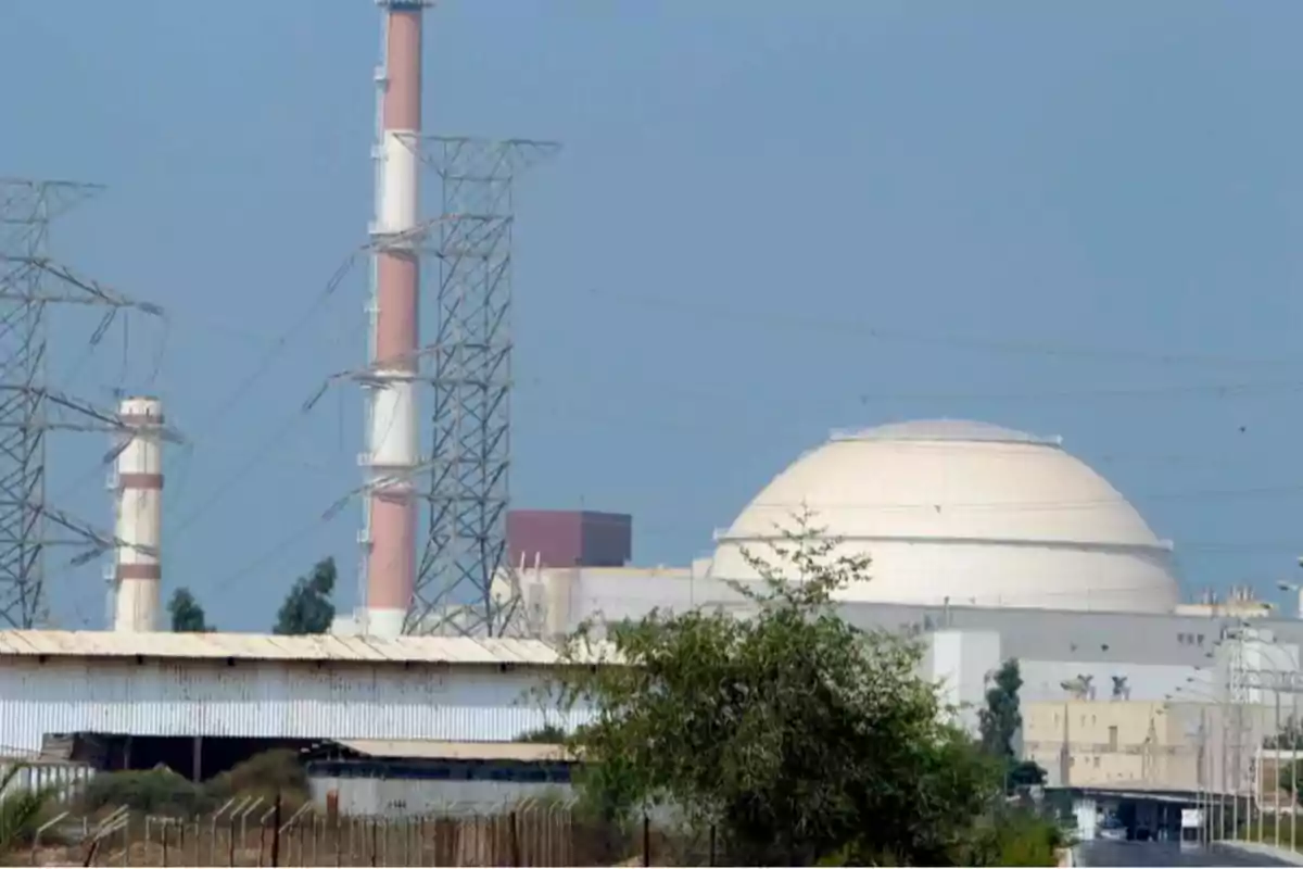 Planta de energía nuclear con cúpula blanca y torres de transmisión eléctrica en un entorno industrial.