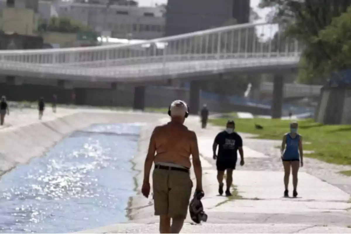 Personas caminando junto a un canal con un puente al fondo.