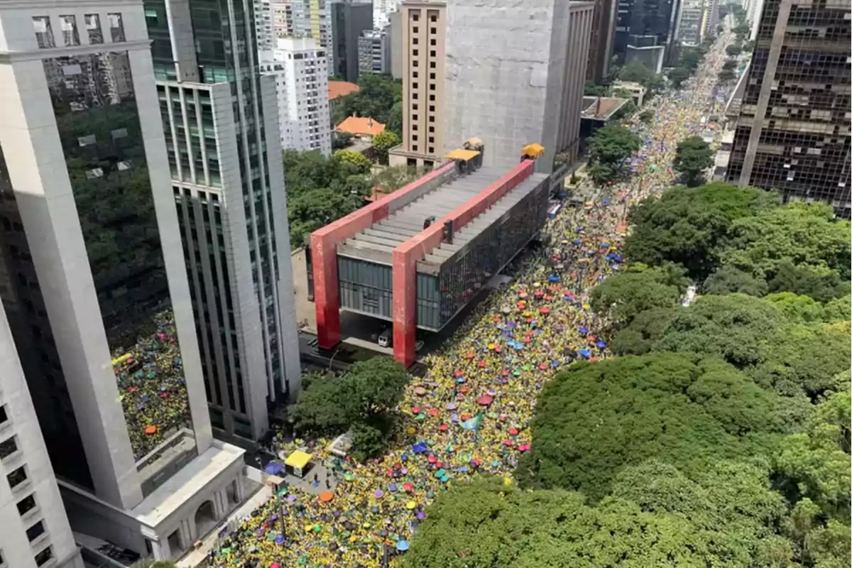 Una multitud de personas se reúne en una avenida rodeada de edificios altos y áreas verdes.