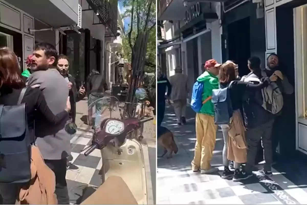 Un grupo de personas interactúa en una calle peatonal, algunas parecen estar discutiendo mientras otras observan, y una motocicleta está estacionada cerca.