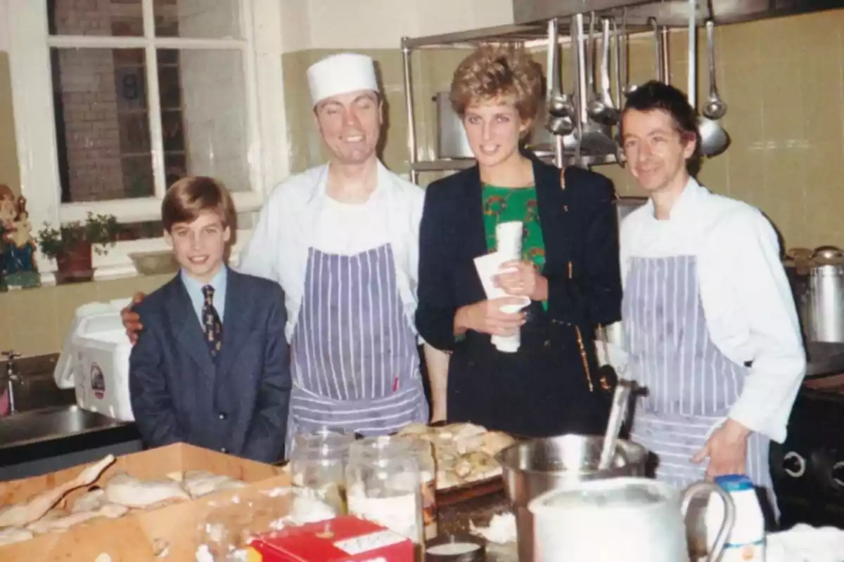 Un niño y una mujer posan con dos chefs en una cocina industrial, con utensilios y alimentos en la mesa.