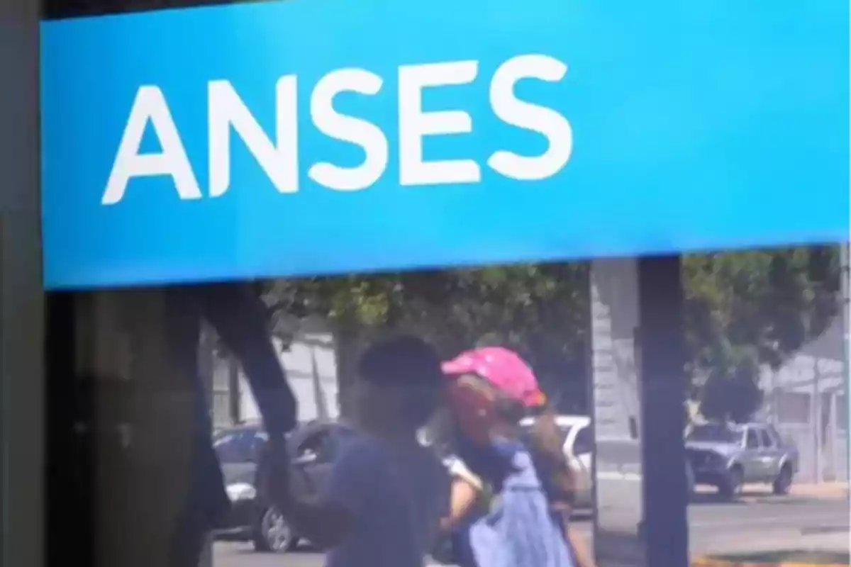 Un cartel azul con la palabra ANSES reflejando a dos personas caminando afuera.