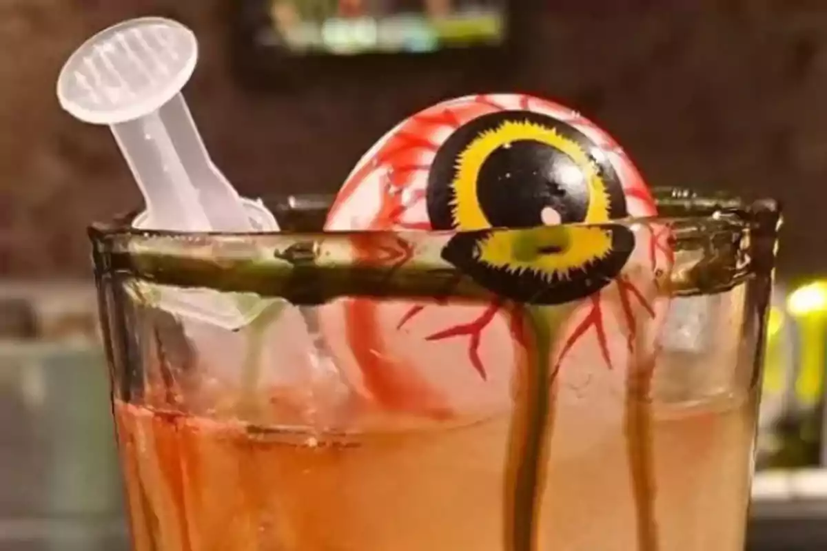 Un vaso con una bebida decorada con un ojo de juguete y una jeringa de plástico.