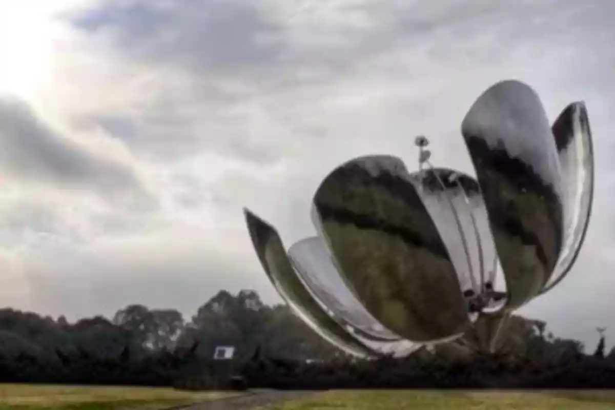 Escultura metálica en forma de flor con pétalos abiertos bajo un cielo nublado.