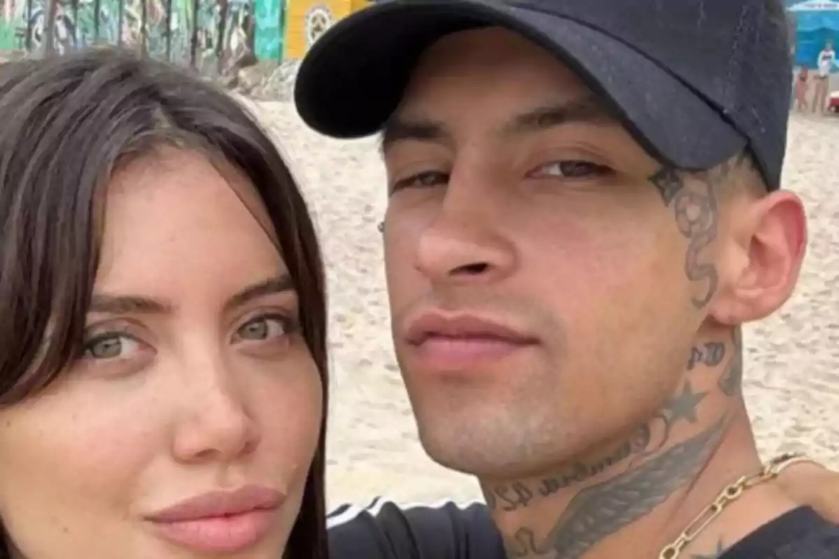 Una pareja joven posando para una selfie en la playa con un fondo de murales coloridos.