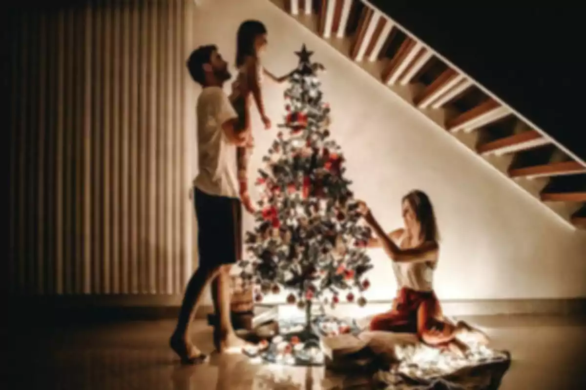 Una familia decorando un árbol de Navidad bajo una escalera en un ambiente cálido y acogedor.