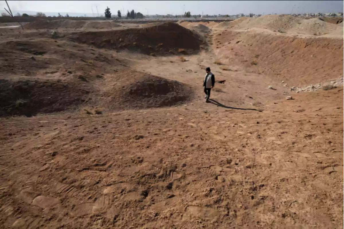 Persona caminando en un terreno árido y polvoriento con colinas bajas al fondo.