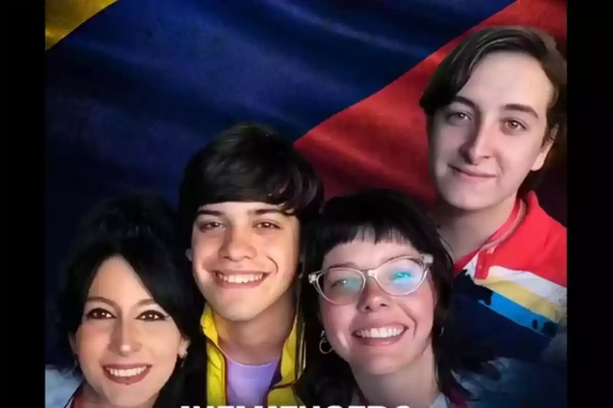 Un grupo de cuatro personas sonrientes posando frente a una bandera colorida.