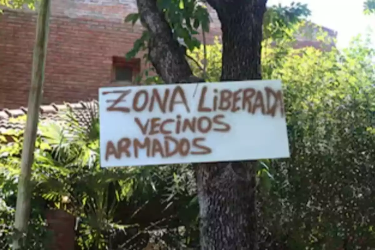 Un cartel colgado en un árbol advierte sobre una zona liberada con vecinos armados.