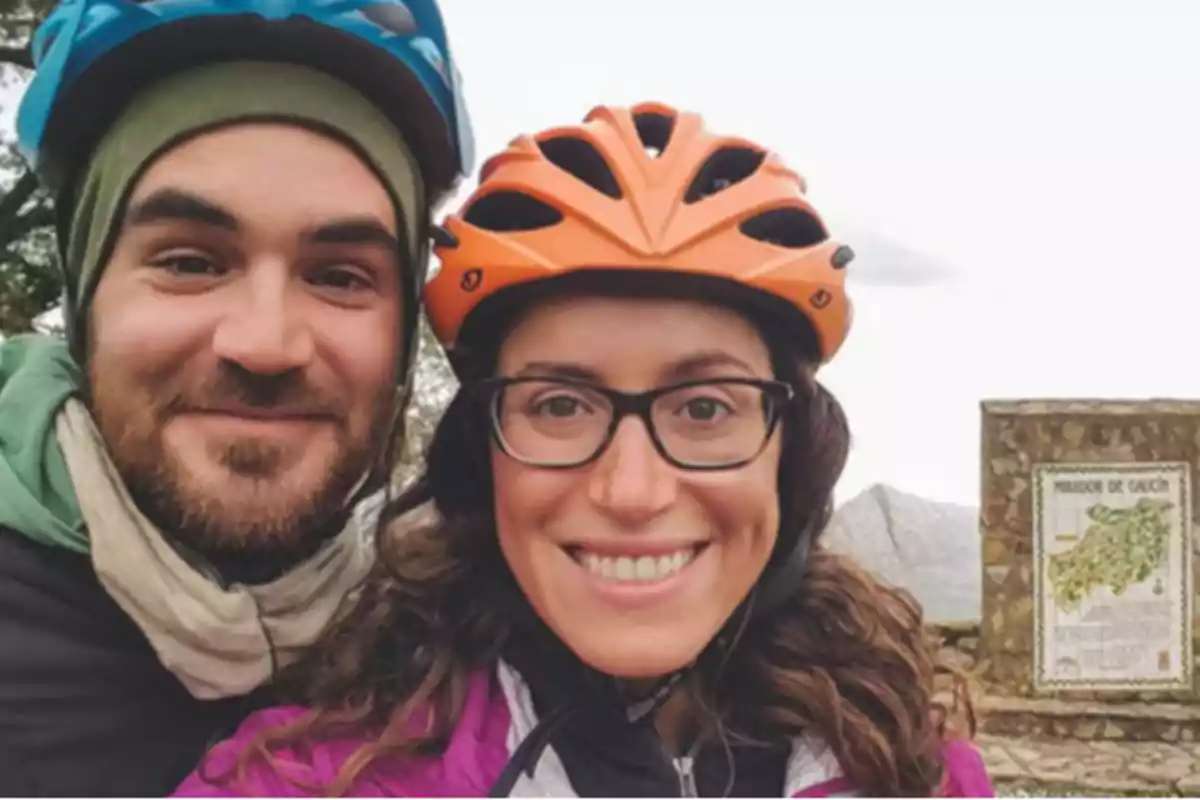 Una pareja sonriente con cascos de bicicleta en un entorno al aire libre.