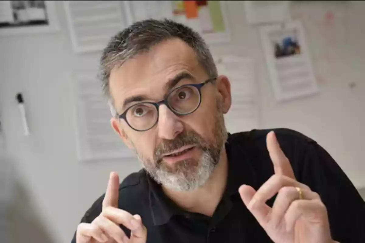 Un hombre con gafas y barba gesticula mientras habla en una oficina.