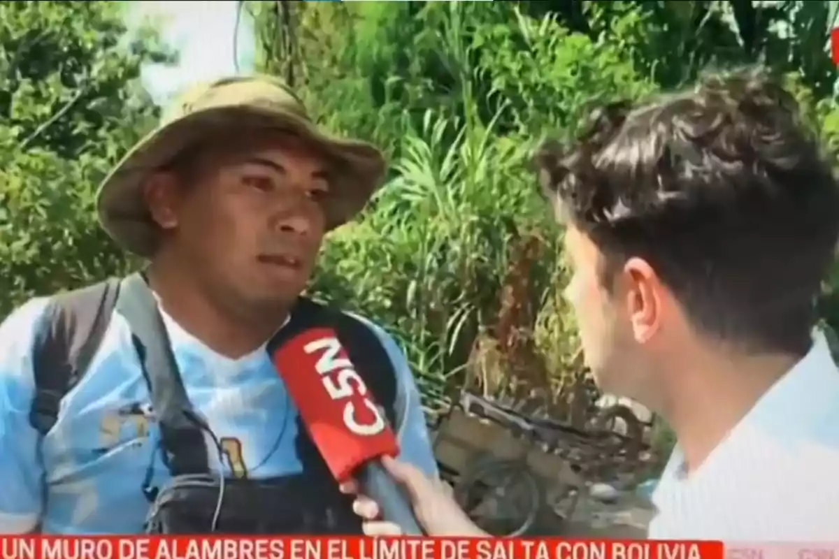 Un reportero de C5N entrevista a un hombre con sombrero en un entorno al aire libre.