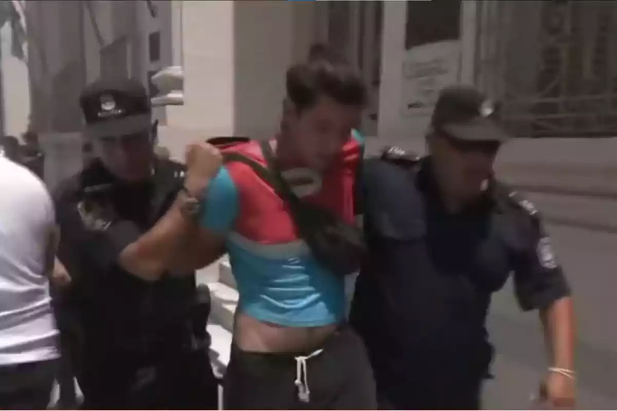 Un hombre es escoltado por dos policías en una calle.