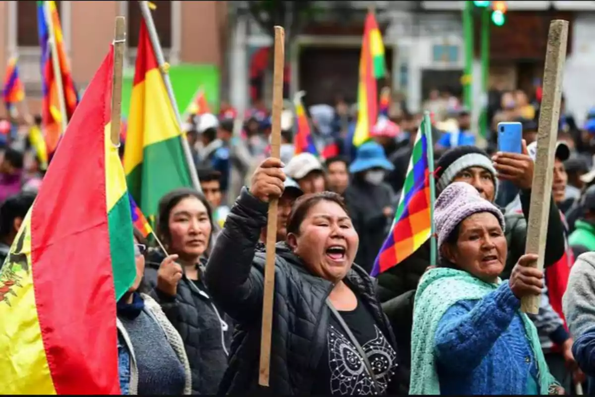 Un grupo de personas participa en una manifestación, sosteniendo banderas y palos, con expresiones de determinación y energía.