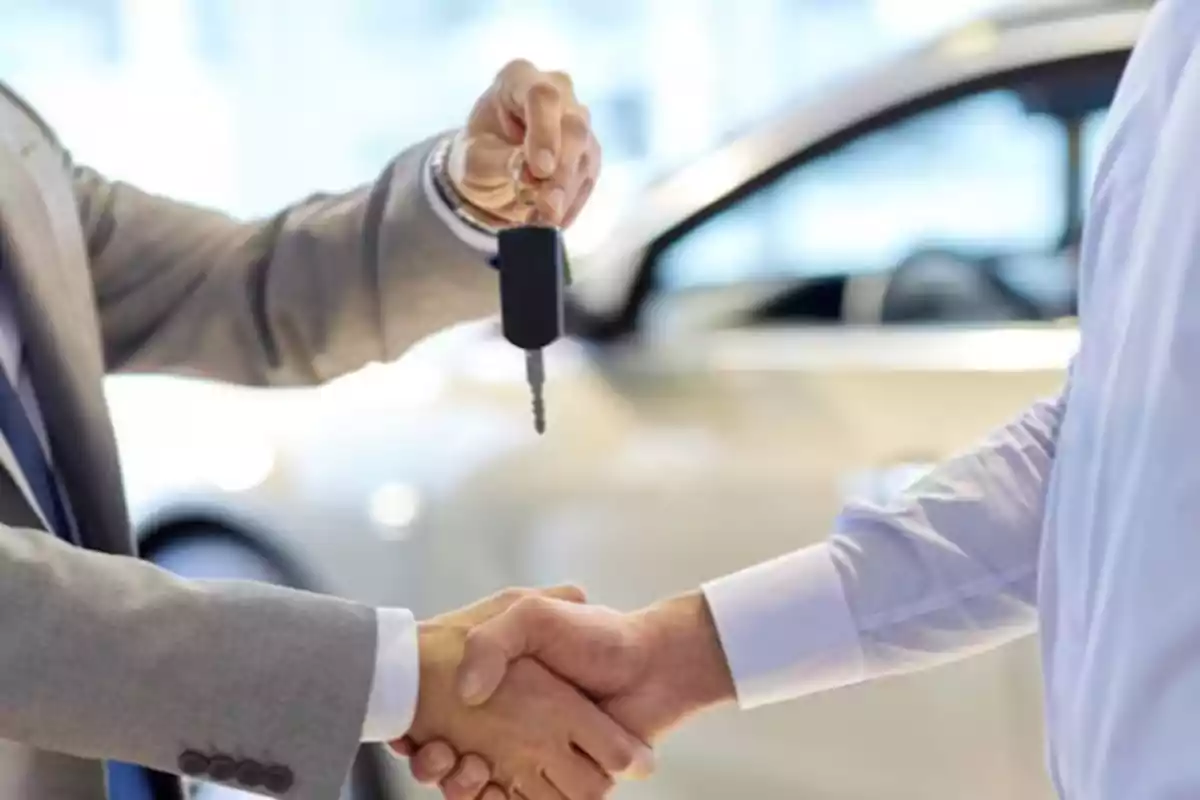 Dos personas dándose la mano mientras una entrega una llave de coche.