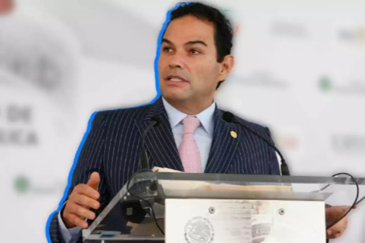 A man in a pinstripe suit speaks at a podium with microphones.