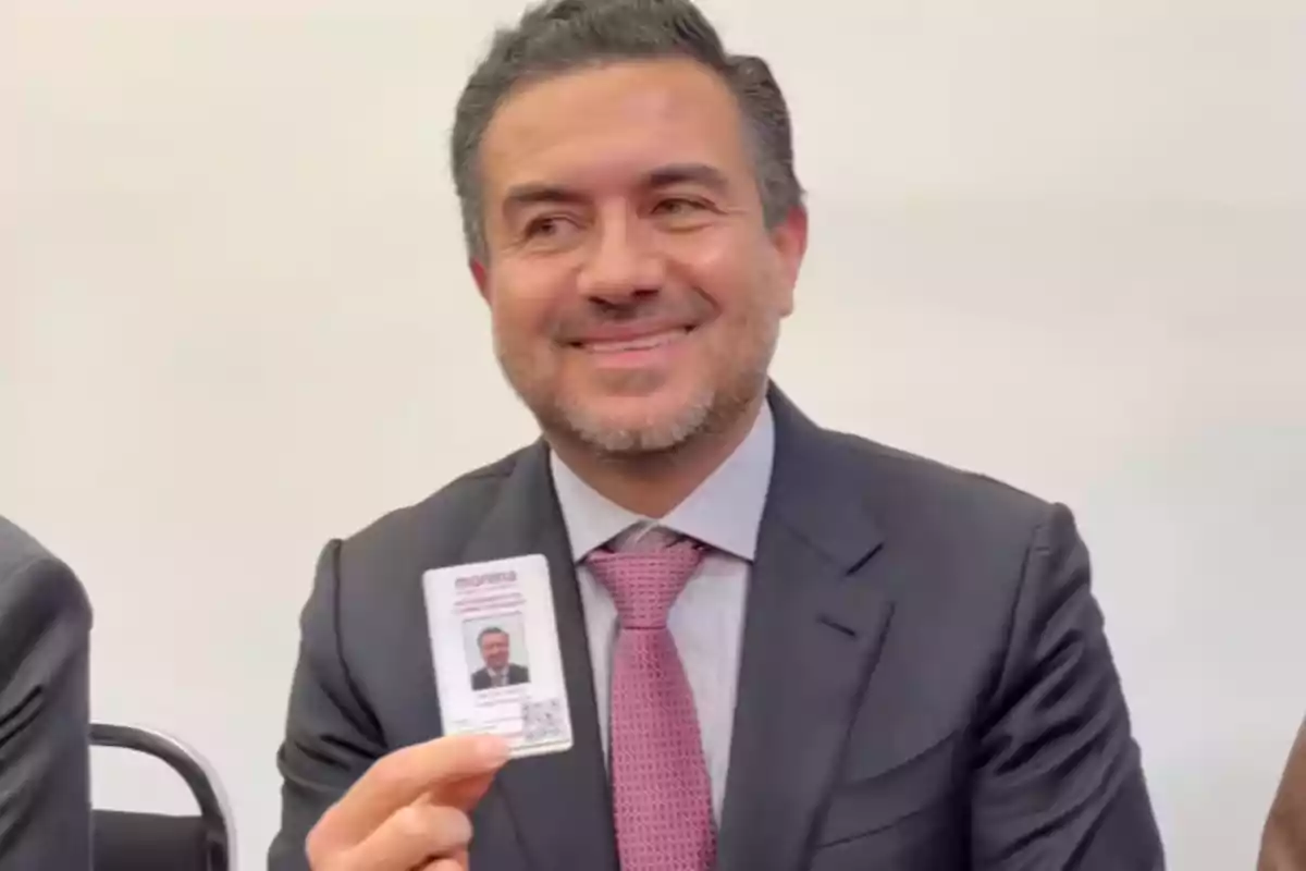 A smiling man in a suit holds a badge in his hand.