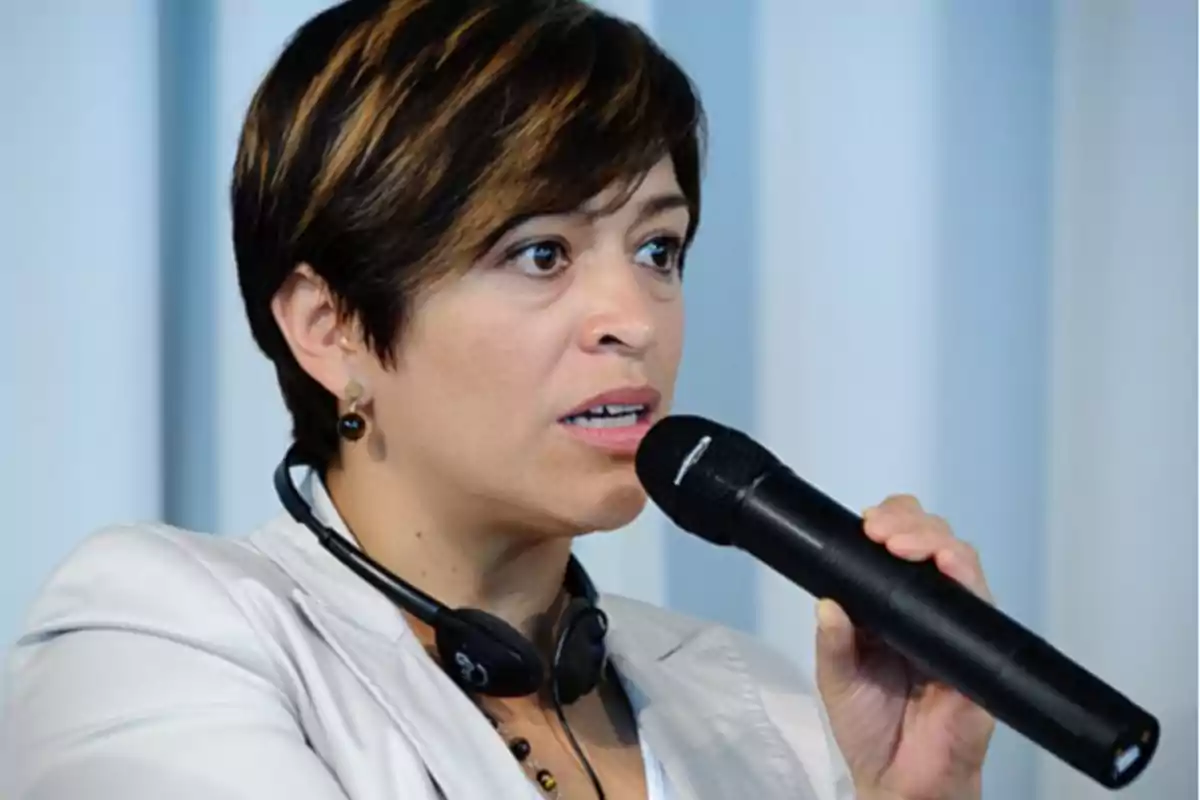 A person speaking into a microphone with headphones around their neck.