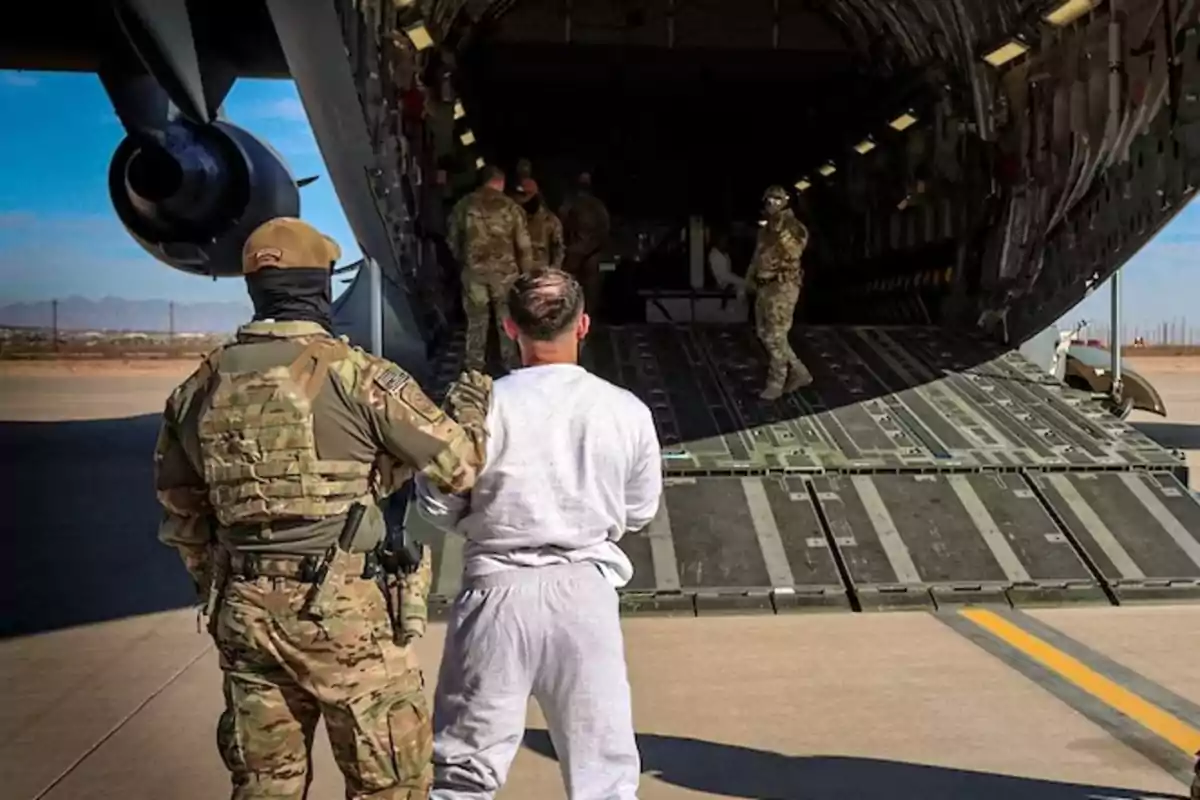 Un grupo de militares escolta a un hombre hacia el interior de un avión de carga en una pista de aterrizaje.