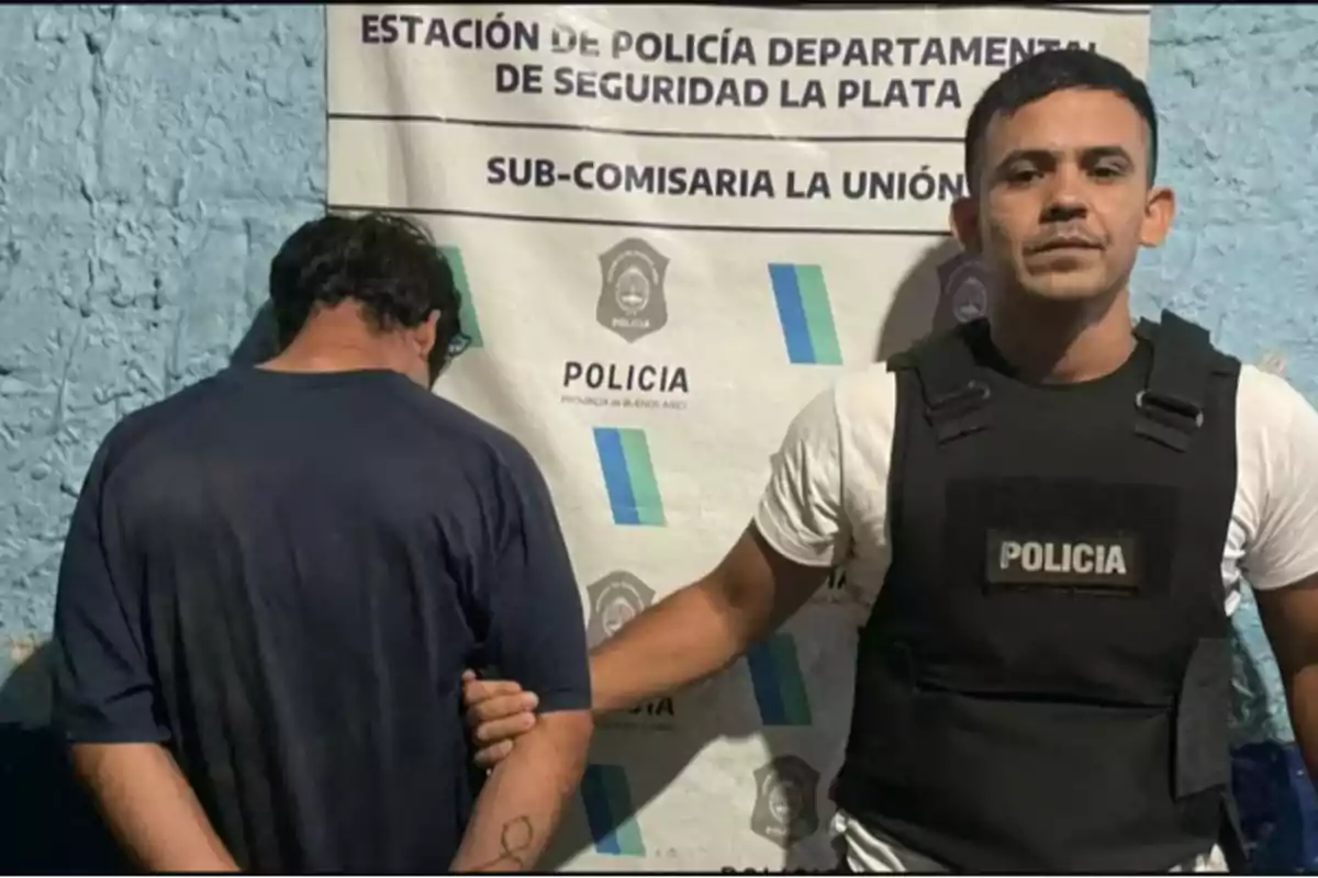 Un policía con chaleco sostiene a un hombre esposado frente a un cartel de la estación de policía de La Plata.