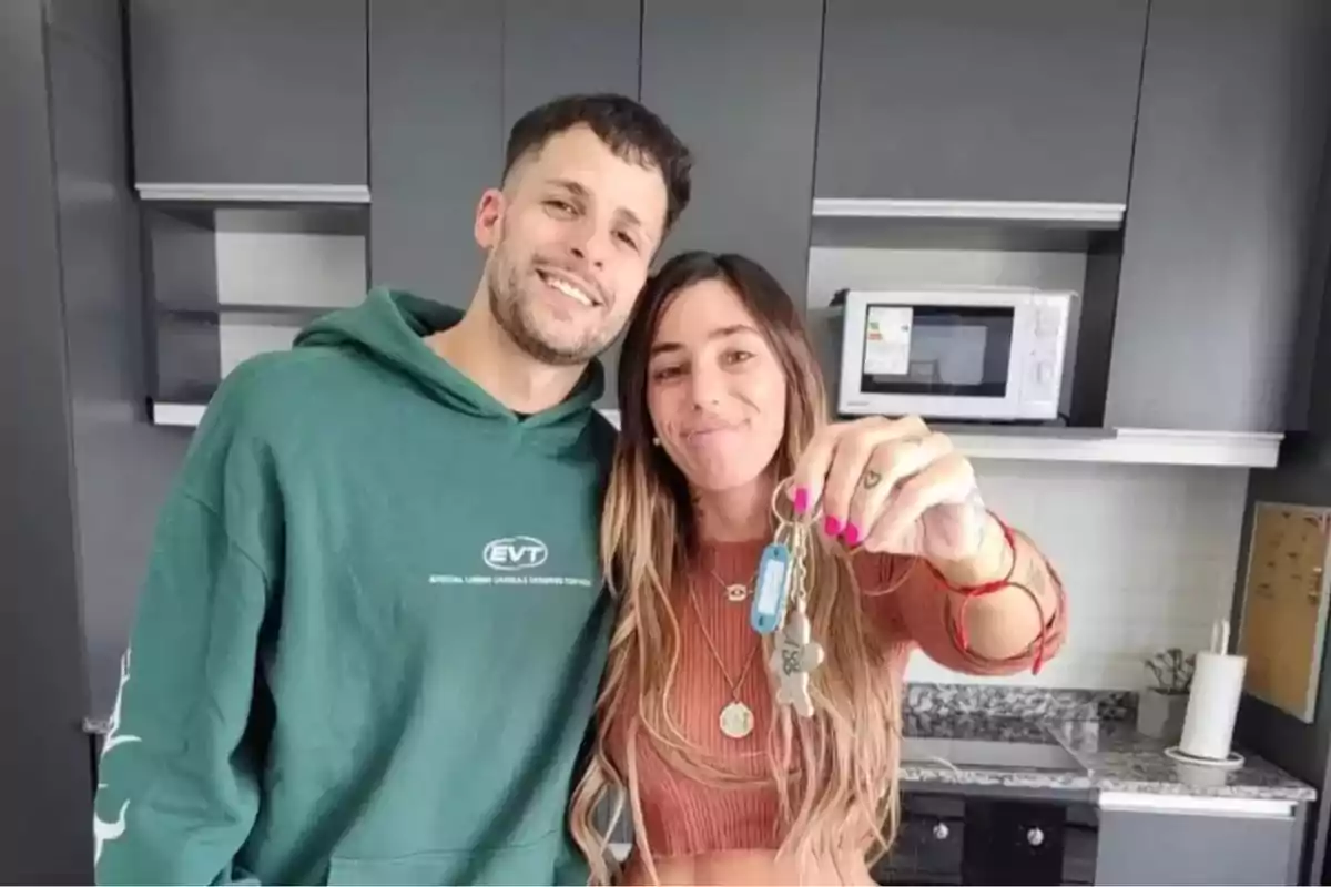 Una pareja sonriente en una cocina moderna mientras la mujer sostiene un manojo de llaves.