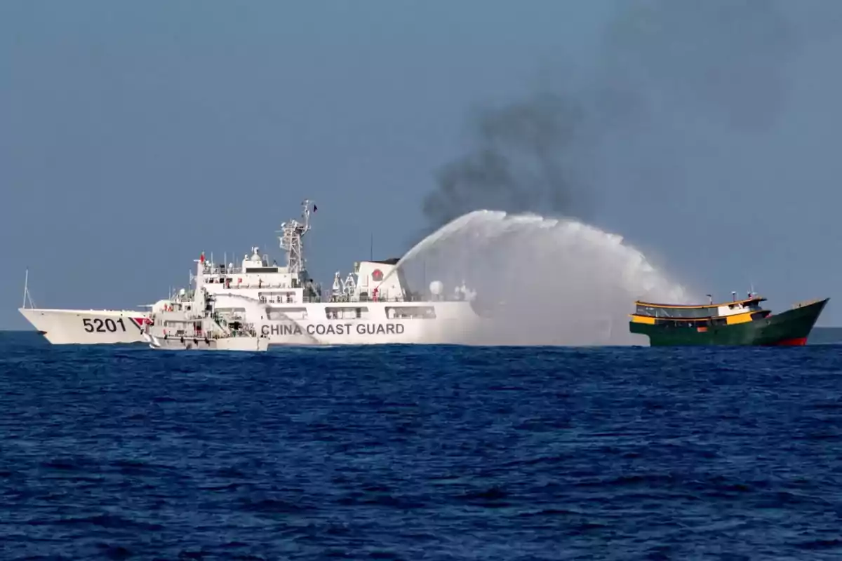 Un barco de la guardia costera china rocía agua hacia un barco más pequeño en el mar.