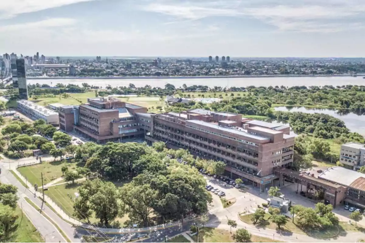 Vista aérea de un campus universitario con edificios de ladrillo rodeados de áreas verdes y un río en el fondo.