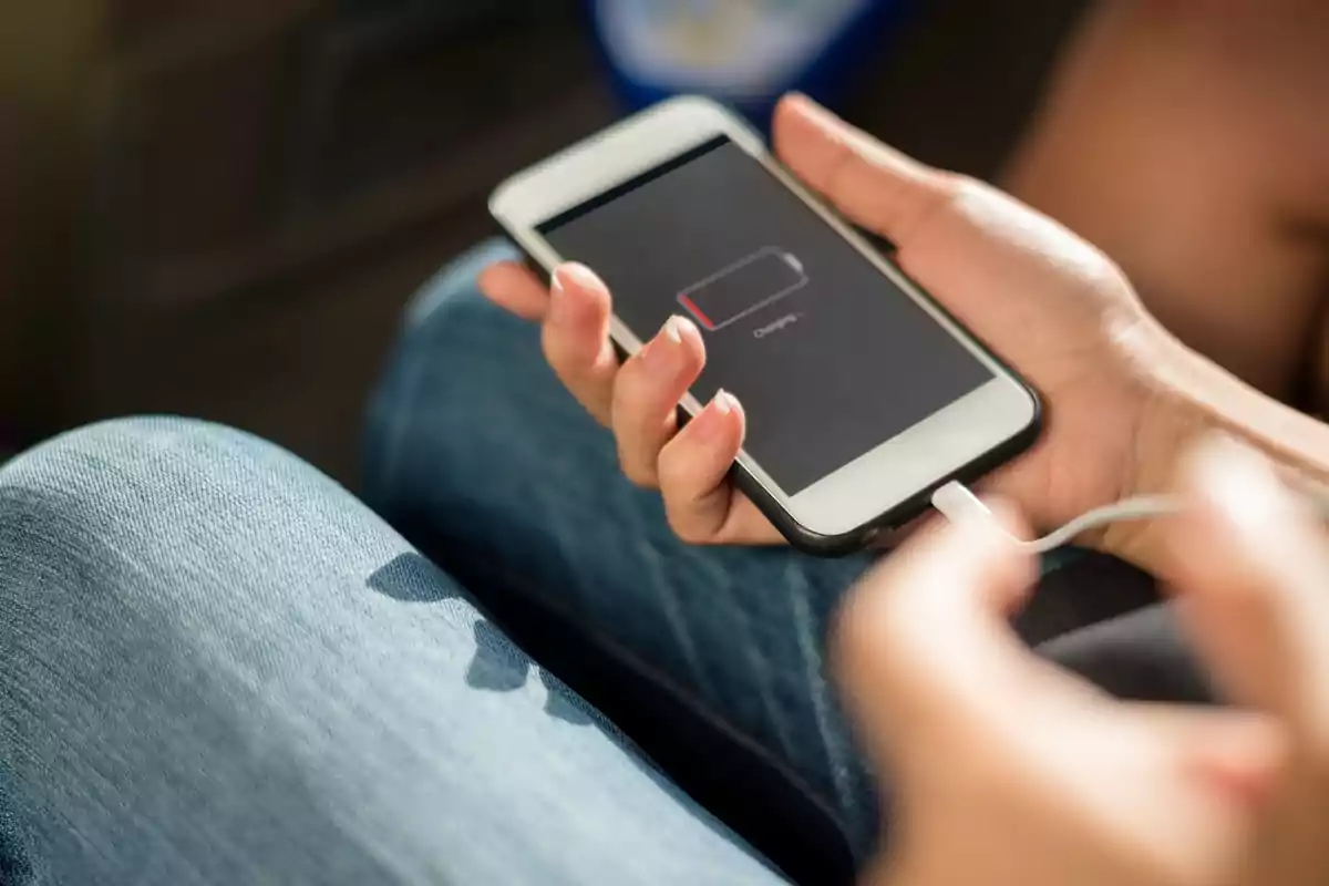 Persona sosteniendo un teléfono móvil con la pantalla mostrando una batería baja mientras está conectado a un cargador.