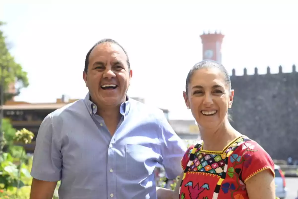 Two smiling people pose outdoors with a historic building in the background.