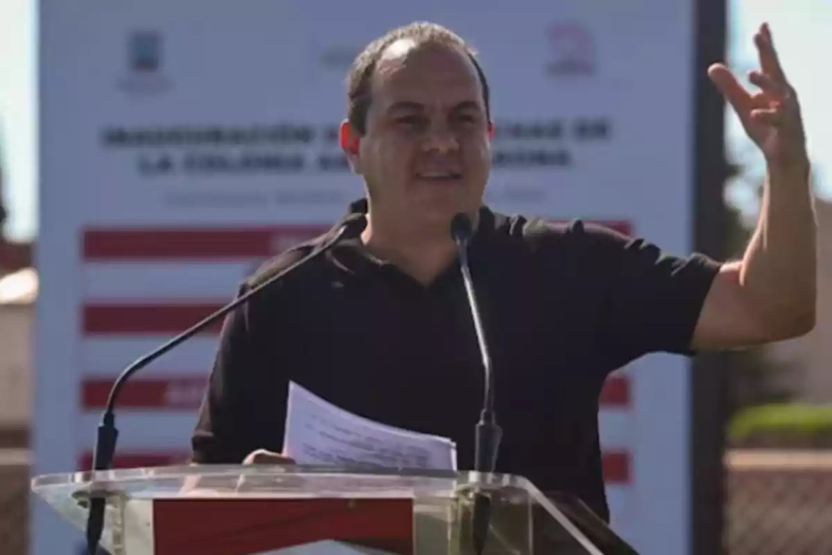 A man speaking at an outdoor podium with a microphone and a blurred background.