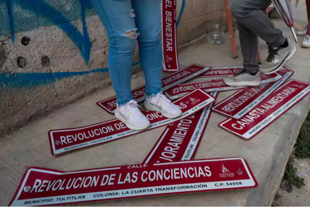 Personas de pie sobre varias placas de calles con nombres relacionados con temas sociales y políticos.