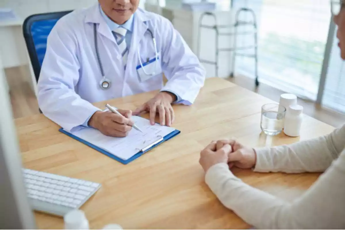 Un médico con bata blanca toma notas mientras conversa con un paciente en una consulta médica.