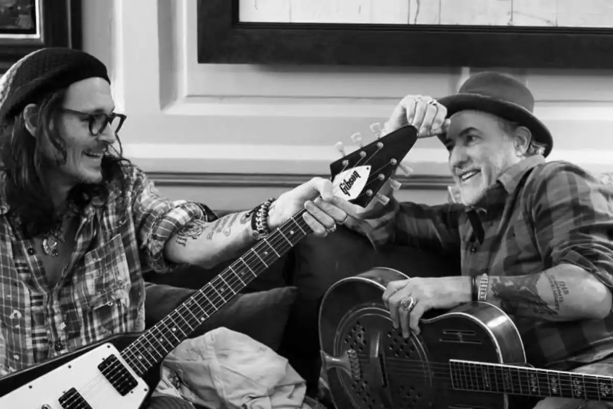 Dos personas sonrientes con guitarras en un ambiente relajado.