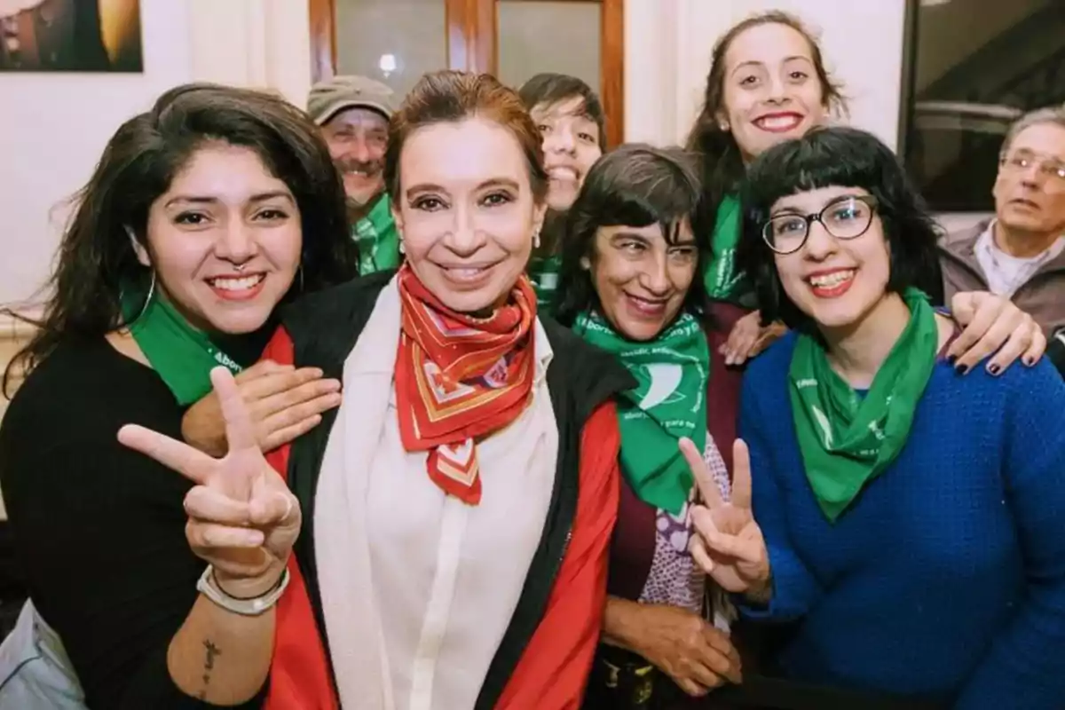 Un grupo de personas sonríe a la cámara, algunas haciendo el signo de la paz, y llevan pañuelos verdes alrededor del cuello.