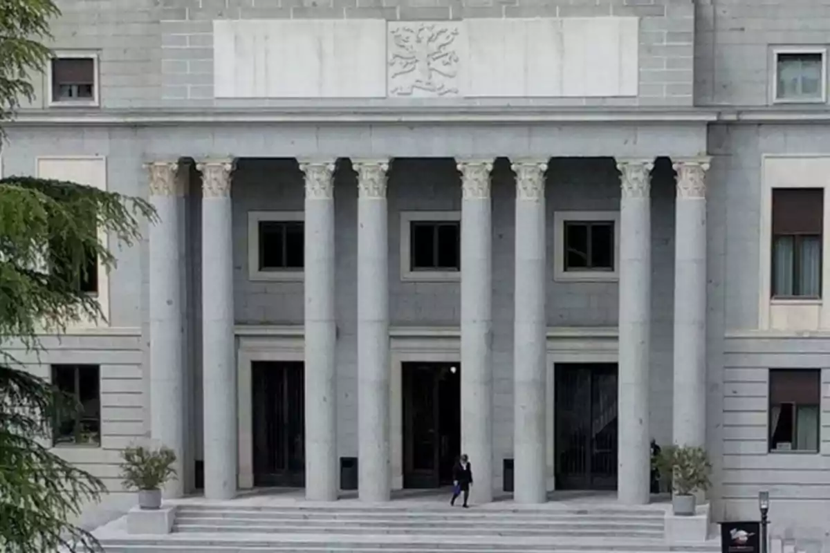 Fachada de un edificio con columnas clásicas y una persona caminando por las escaleras.