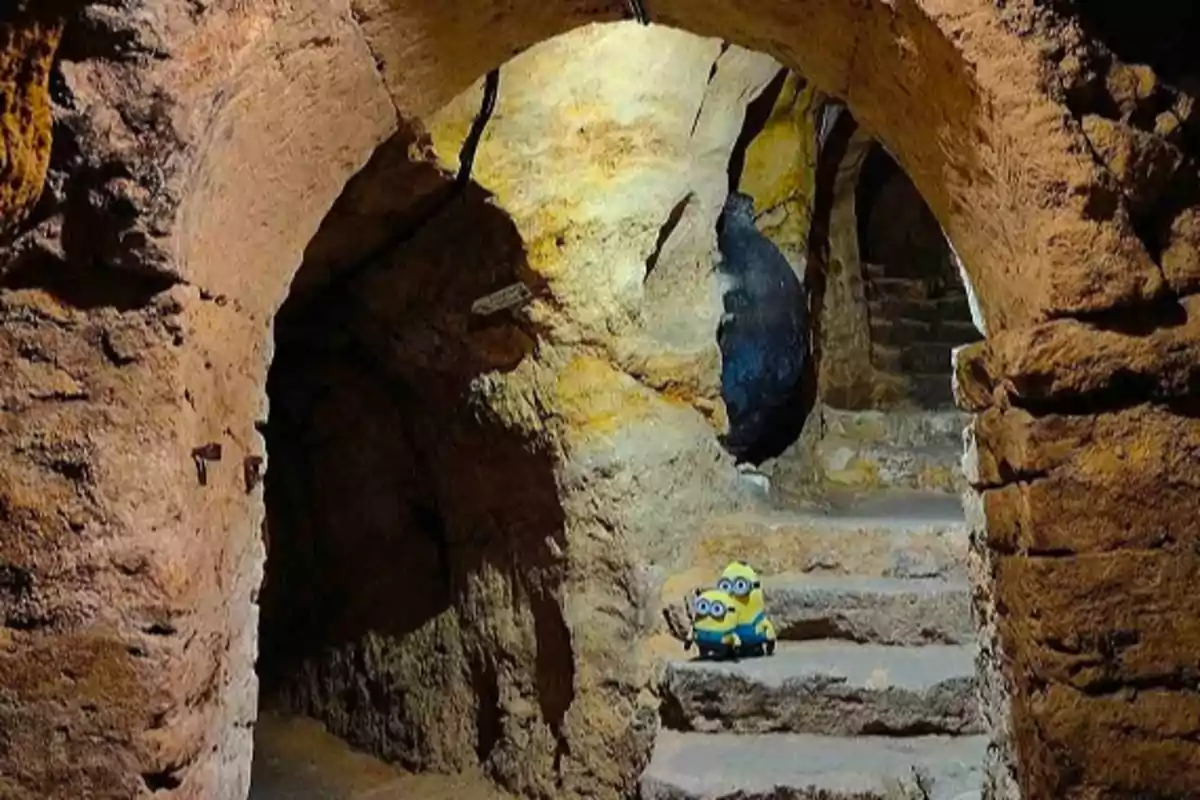 Un par de figuras de Minions se encuentran en una escalera de piedra dentro de una cueva iluminada.