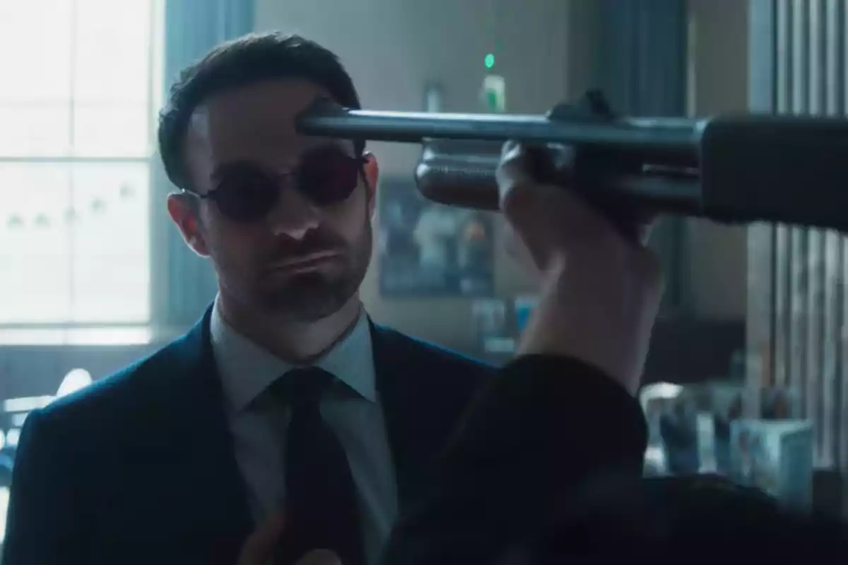 Daredevil de traje está frente al cañón de una escopeta en una habitación iluminada, en la nueva serie "Daredevil: Born Again" de Disney+.