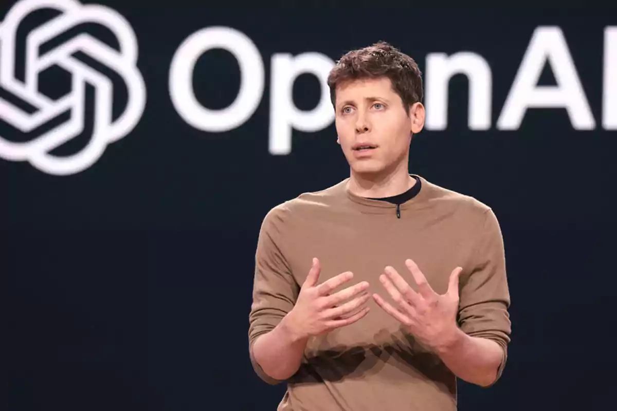 Un hombre hablando en un escenario con el logotipo de OpenAI de fondo.